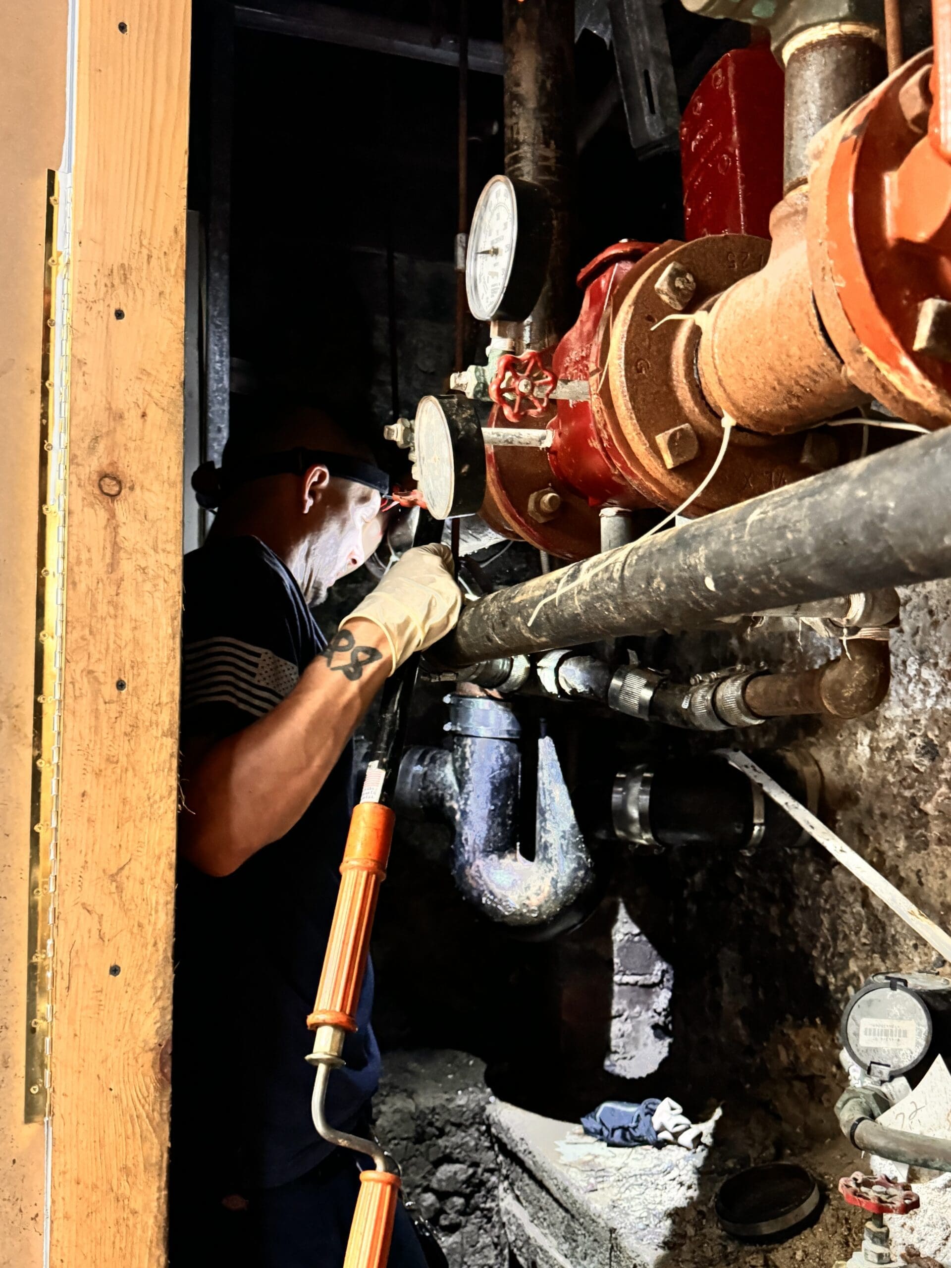 The person is wearing gloves and a headlamp, focused on adjusting or inspecting a pipe system with pressure gauges.