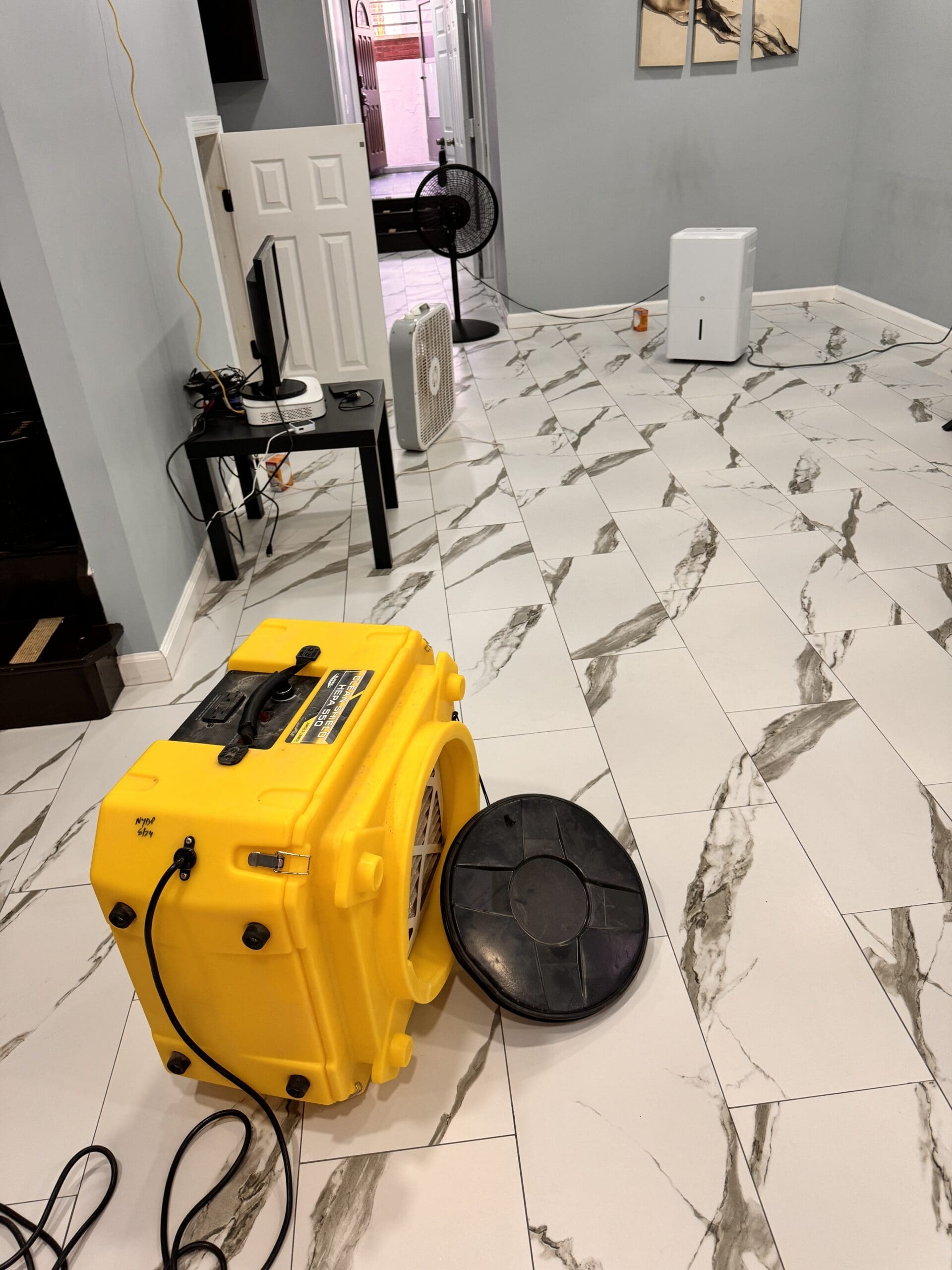 A large yellow air mover or industrial blower is positioned on the floor, with its cover removed and lying next to it.